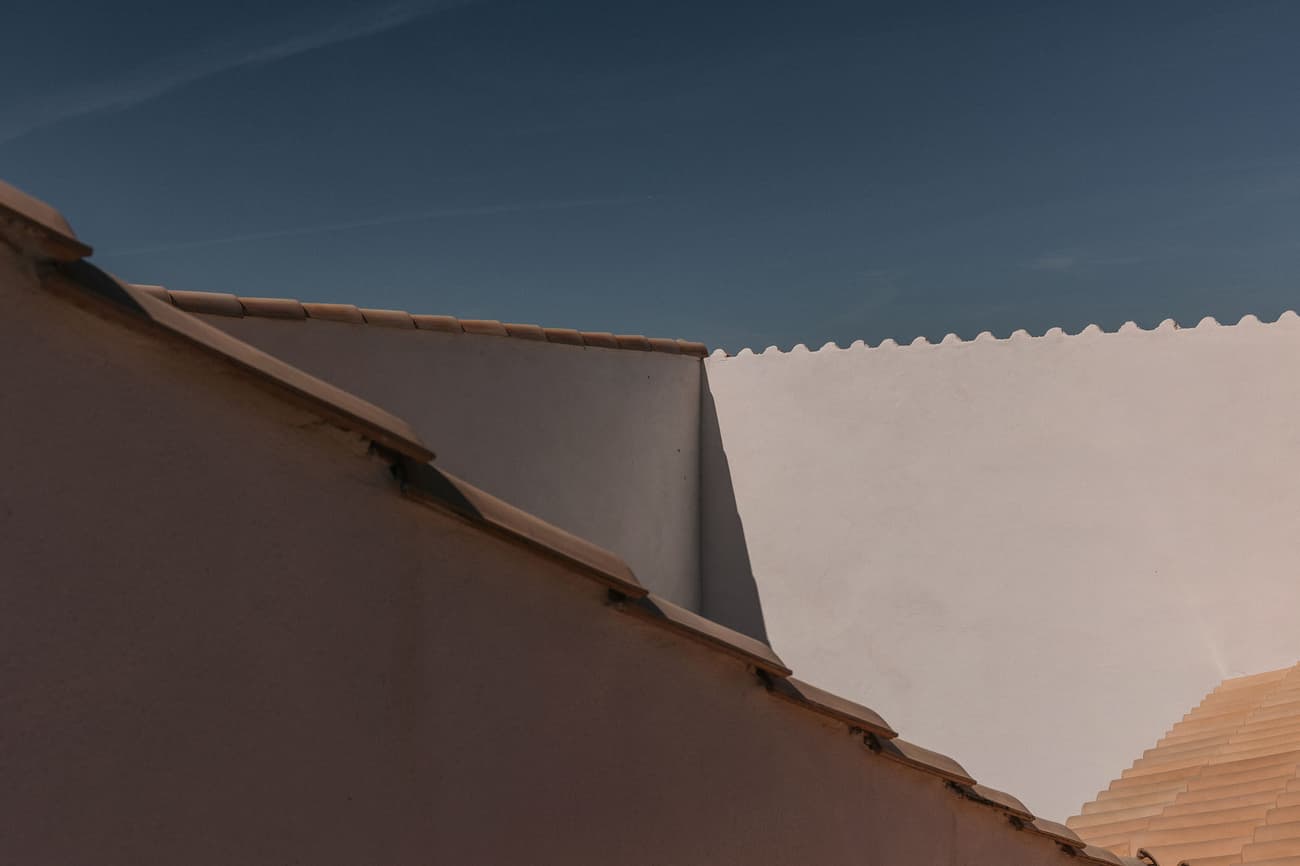 Architectural project - angular design, tan, southern style, terracotta roof, geometric forms, architectural shot, light angles, soft shadows, play of light, roof pattern, smooth surface, white wall, tan roof, outdoor perspective, sunlit exterior, natural materials, Mediterranean influence, natural light, neutral tones, beige, roof detail, minimalist design, contemporary home, modern facade, clean lines, architectural simplicity, white, plaster, earthy tones, clay, sloped roof, plaster finish, terracotta, exterior view, residential architecture, modern home, warm exterior, sharp lines, clay tiles, ceramic, ceramic tiles, exterior cladding
