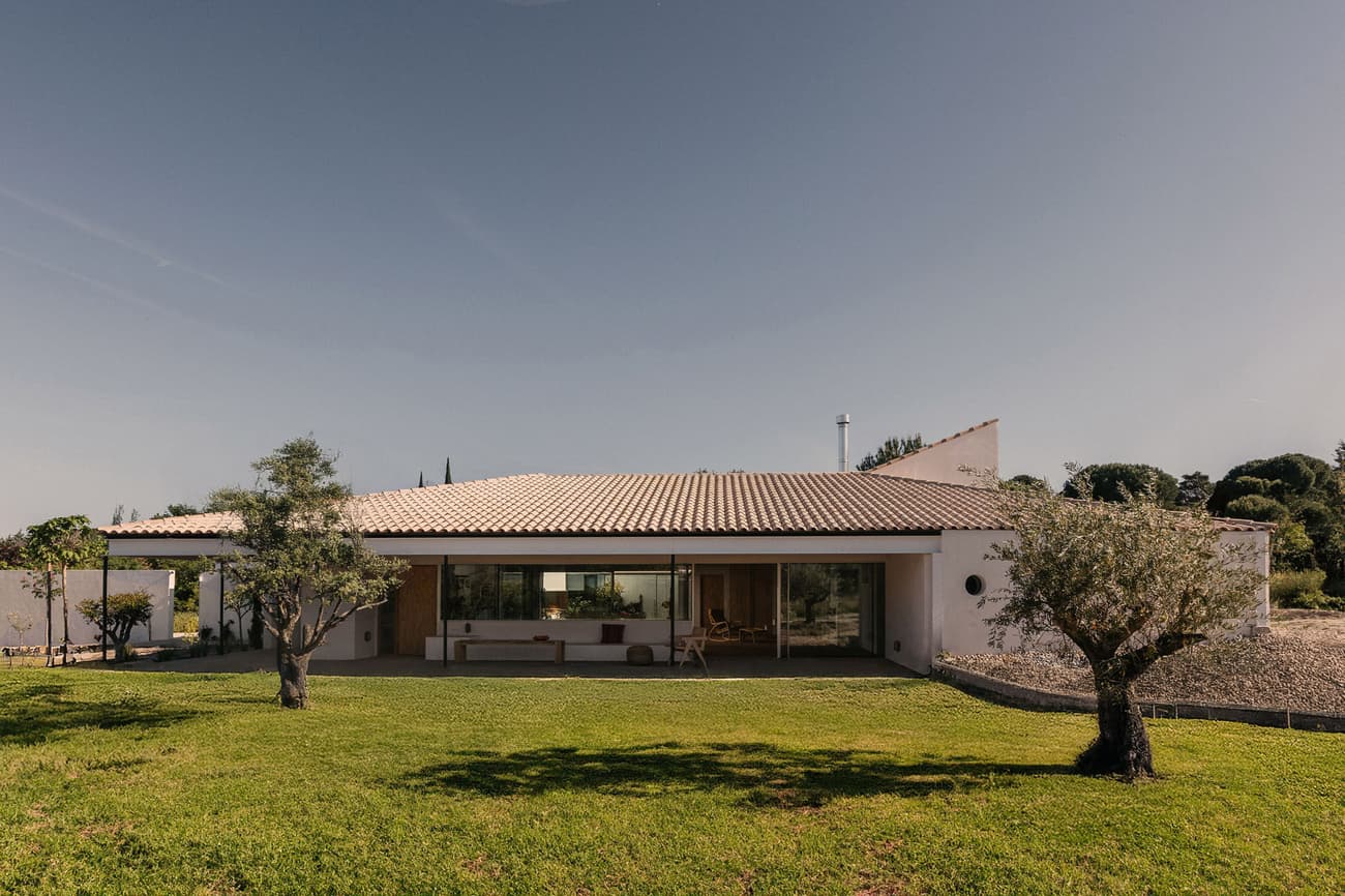 Architectural project - minimalist home, landscape, garden, modern villa, olive trees, masonry, single-story home, ceramic roof tiles, large patio, covered terrace, veranda, escape house, soft lines, expansive lawn, tree-lined, sandstone, natural materials, pastel tones, wood, timber, relaxed vibe, natural light, outdoor living, sustainable design, glass, outdoor area, grey, green, beige, daylight optimization, natural setting, exterior, open facade, natural landscape, passive house, white facade, large windows, white, eco friendly home, countryside home, energy efficient, plaster, beige tones, clay, pitched roof, Mediterranean style, warm climate, nature retreat, greenery, garden view, residential architecture, cozy exterior, vacation home, family home, modern home, seamless transition, green lawn, glass facade, warm materials, indoor outdoor flow, rural house, serene home, ceramic