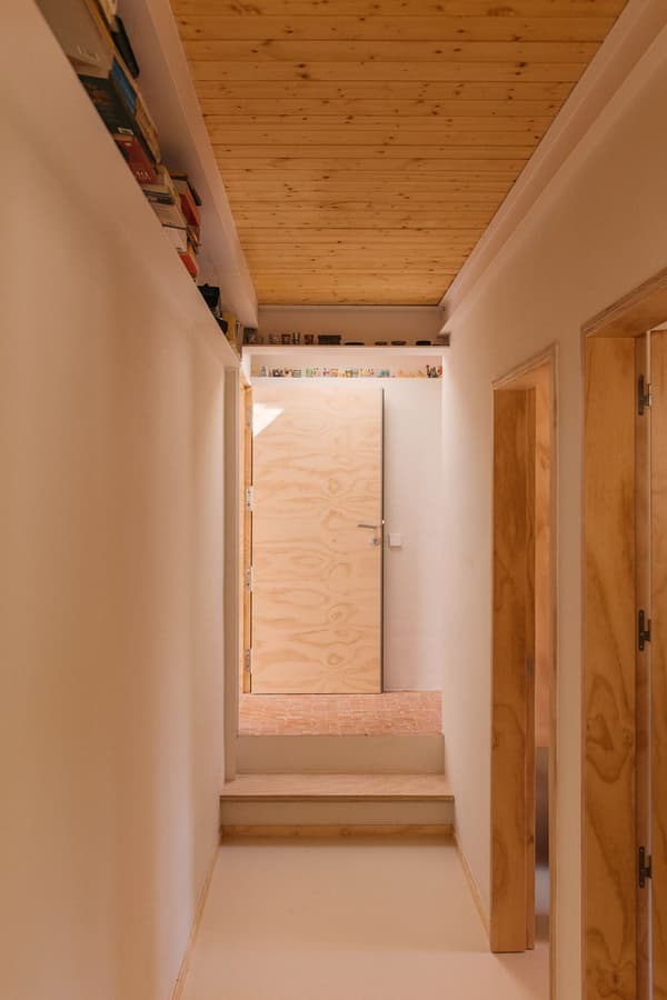 Architectural project - passageway, wooden hallway, cozy hallway, plank ceiling, bookshelf, built-in shelf, entrance, inviting, open hallway, doorway, interior door, wood panel door, plywood door, light palette, soft lighting, sustainable materials, wood, timber, casual style, natural light, warm tones, contemporary style, neutral tones, functional space, daylight, plywood, beige, light wood, natural wood, eco friendly, simple design, light filled, cozy vibe, architectural details, Nordic style, small space, timber ceiling, compact design, warm atmosphere, Scandinavian design, wall shelf, efficient layout, residential, wood ceiling, home interior, minimal decor, interior design, home corridor, corridor, hallway, minimalist hallway, modern interior, bright, airy