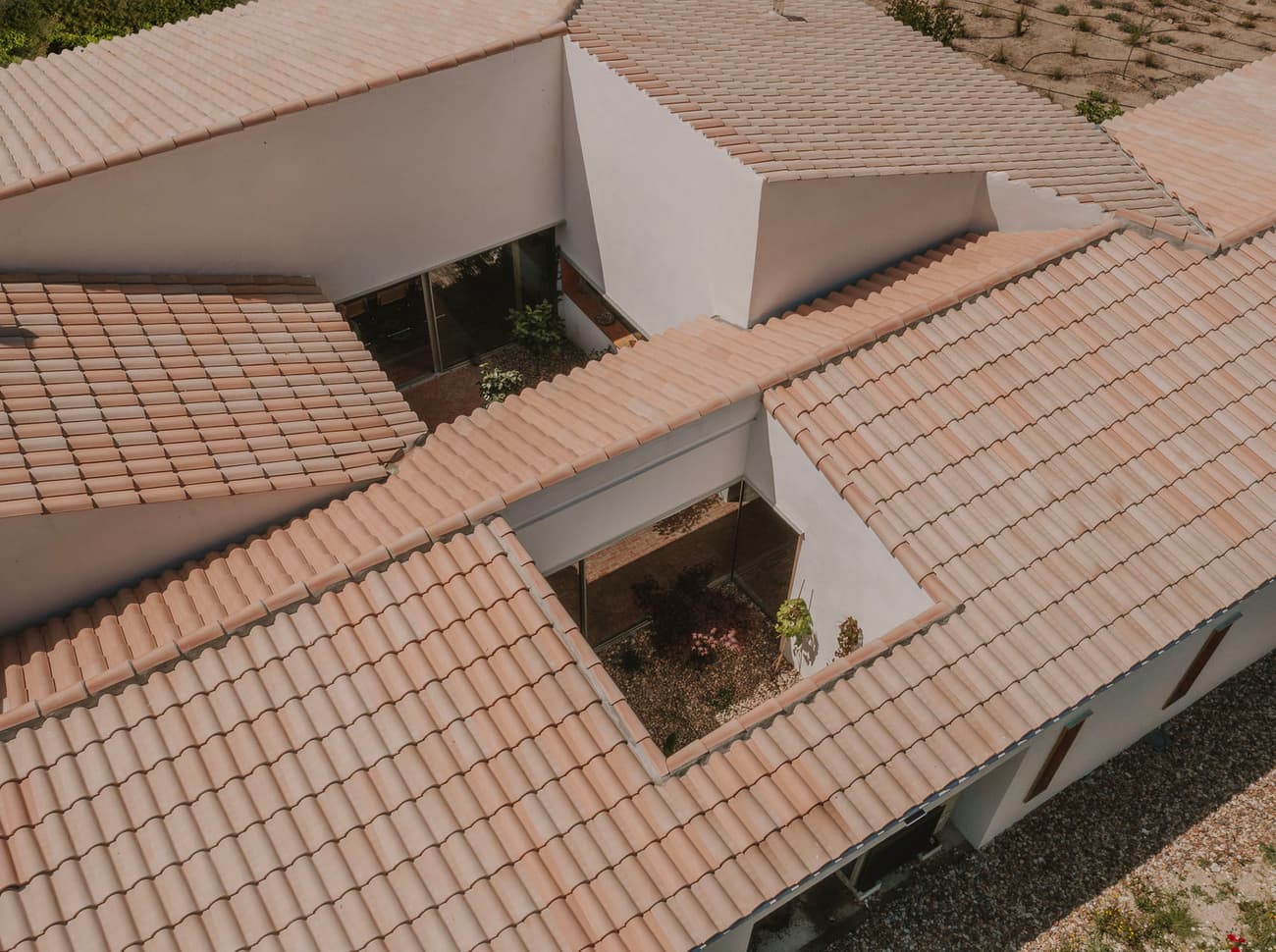 Architectural project - minimalist house, tiled roof, terracotta roof, geometric forms, roof pattern, open courtyard, central courtyard, angled roof, plaster facade, plaster exterior, linear forms, flat layout, light earth tones, beige tiles, layered roof, protective roof, modern roof, shaded areas, house layout, architectural layout, minimal design, natural materials, outdoor space, passive design, warm tones, eco design, sustainable architecture, neutral tones, geometric design, natural ventilation, contemporary home, white facade, modern architecture, earthy tones, pitched roof, residential design, gable roof, white exterior, horizontal design, courtyard, exterior space, clay tiles, ceramic tiles, garden space, suburban house