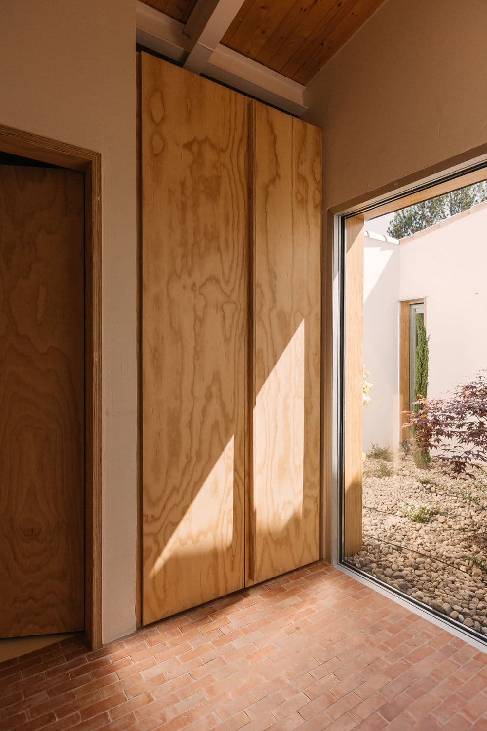 Architectural project - terracotta tiles, garden integration, courtyard view, pocket garden, japandi vibe, small courtyard, privacy wall, textured flooring, brick floor, intimate space, natural materials, architectural detail, soft lighting, wood, timber, raw materials, natural light, sustainable design, warm tones, contemporary style, daylight, plywood, beige, light wood, golden, Scandinavian influence, sunlight, natural textures, neutral palette, minimalist design, relaxed atmosphere, modern minimalism, clean lines, light filled, indoor outdoor, white, eco friendly home, textured wall, plaster wall, plaster, cozy nook, earthy tones, terracotta, cozy corner, residential architecture, bright interior, modern home, home design, passive solar, open space, simple lines, timber paneling, timber door, wooden door