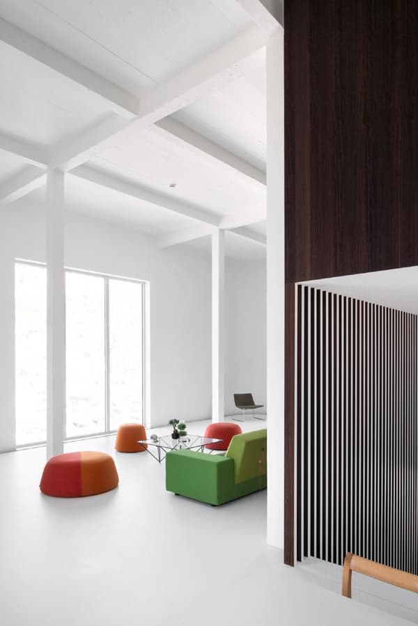 Architectural project - lounging area, modern decor, colorful furniture, vibrant seating, simplicity, green sofa, orange pouf, red pouf, striped accents, eco-friendly design, wood, timber, natural light, green, neutral tones, ceiling beams, daylight, gathering space, spacious layout, brown, modern aesthetic, functional design, casual seating, social space, relaxed atmosphere, orange, clean lines, white walls, white, Nordic style, large window, cozy corner, modern living room, Scandinavian design, bright interior, sleek design, home design, open space, contemporary vibe, airy feel, vertical slats, wood paneling, minimalist interior, residential interior, red