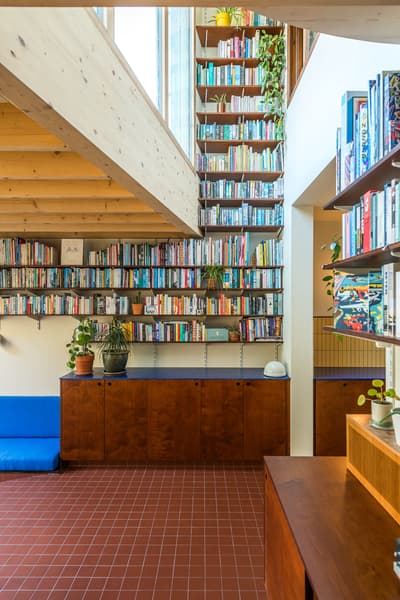 Architectural project - efficient use, indoor greenery, home decor, red floor, eclectic vibe, casual atmosphere, terracotta tiles, farmhouse modern, book storage, open library, tall shelves, floor-to-ceiling shelves, colorful books, warm interior, wood, timber, natural light, warm tones, neutral tones, daylight, light wood, natural wood, wooden beams, industrial touch, Scandinavian style, neutral palette, vibrant space, eco-friendly materials, creative space, modern rustic, biophilic design, sustainable home, white walls, Nordic design, timber ceiling, comfortable home, inviting space, terracotta, cozy corner, reading nook, built-in shelves, reading area, home library, compact living, residence, cozy home, interior design, educational space, ceramic, skylight, indoor plants, double height, bright room, exposed ceiling