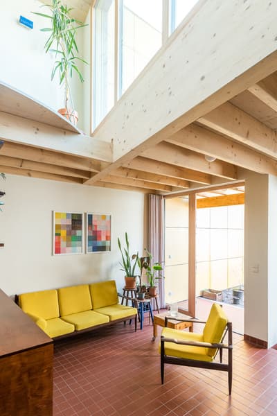 Architectural project - open ceiling, retro vibe, living room, indoor garden, plant decor, sitting area, Nordic touch, houseplants, airy room, mid-century style, vintage furniture, tile floor, yellow sofa, colorful art, warm room, yellow chairs, relaxation space, natural materials, wood, timber, natural light, sustainable design, yellow, glass, warm tones, neutral tones, daylight, beige, brown, wooden beams, timber beams, Scandinavian style, glass doors, cozy space, eco friendly home, inviting home, open plan, terracotta, outdoor connection, residential space, bright interior, lounge area, sliding doors, home design, comfortable living, family room, open space, modernist style, green materials, terracotta floor, art wall, double height, exposed ceiling