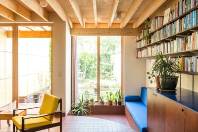 Architectural project - hygge vibe, living room, terracotta tiles, plant shelf, minimalist furniture, bookshelf, blue bench, relaxation space, natural materials, wood, timber, natural light, passive design, sustainable design, yellow, warm tones, green, neutral tones, exposed beams, daylight, brown, light wood, blue, wooden beams, honey wood, rustic modern, Scandinavian style, modern rustic, indoor outdoor, white, Nordic design, eco friendly home, cozy vibe, cozy nook, timber ceiling, open shelves, casual living, open layout, inviting space, warm atmosphere, terracotta, garden view, reading nook, comfortable seating, home library, bright interior, built-in seating, wood ceiling, terracotta floor, ceramic, indoor plants