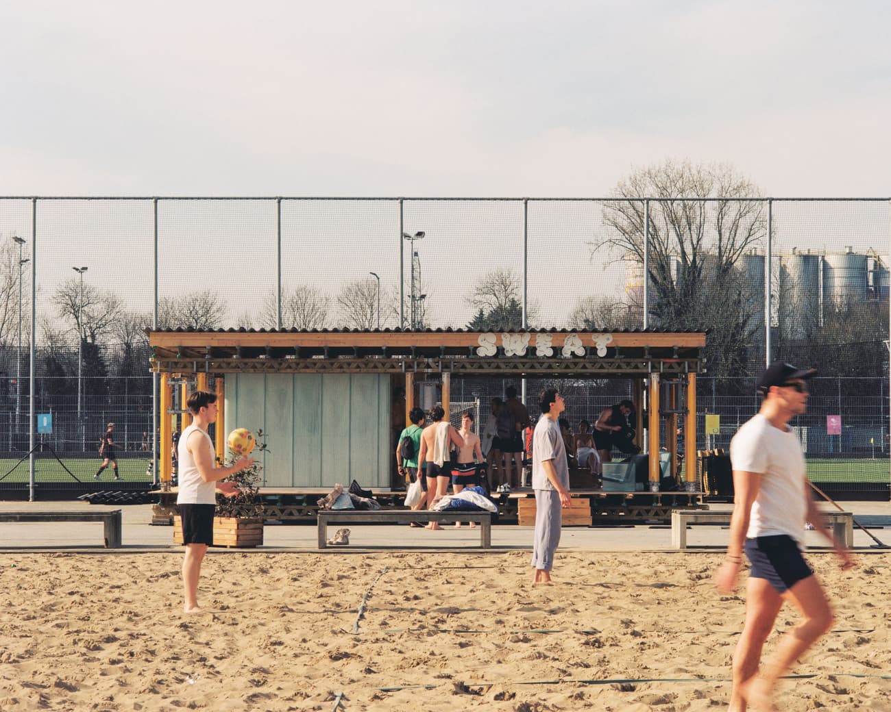 Architectural project - wood, timber, temporary structure, outdoor living, neutral tones, sports field, recreational area, beige, light wood, open structure, urban oasis, timber construction, outdoor, leisure space, beach cafe, outdoor cafe, sandy area, casual seating, social space, community hub, beach vibe, relaxed atmosphere, wooden pavilion, youth gathering, urban beach, pop-up cafe, seasonal design, beachside design, summer destination, active lifestyle, playful environment, informal setting, seaside retreat, summertime spot, urban recreation, sports leisure, minimal structure, open framework, daytime hangout, casual environment, outdoor pavilion, public amenity, relaxation spot, sports ground, casual gathering, temporary pavilion, sand, exterior