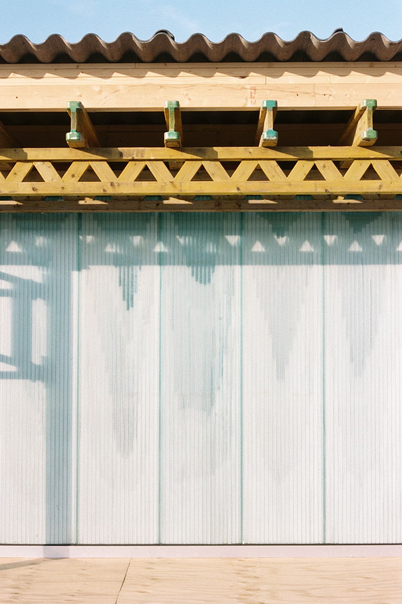 Architectural project - light blue, natural materials, architectural detail, eco-friendly design, wood, timber, raw materials, steel, metal, outdoor space, shadow play, natural tones, corrugated roof, contemporary architecture, sustainable architecture, neutral tones, modern construction, daylight, beige, wood facade, timber facade, truss structure, exposed trusses, light and shadow, wavy roof, architectural elements, structural design, roof design, roof detail, timber detail, wooden trusses, timber trusses, exterior design, building facade, architectural facade, minimal aesthetics, minimalist facade, geometric pattern, visual rhythm, light wood, natural wood, exterior wall, open air design, modern aesthetic, architectural photography, building design, golden