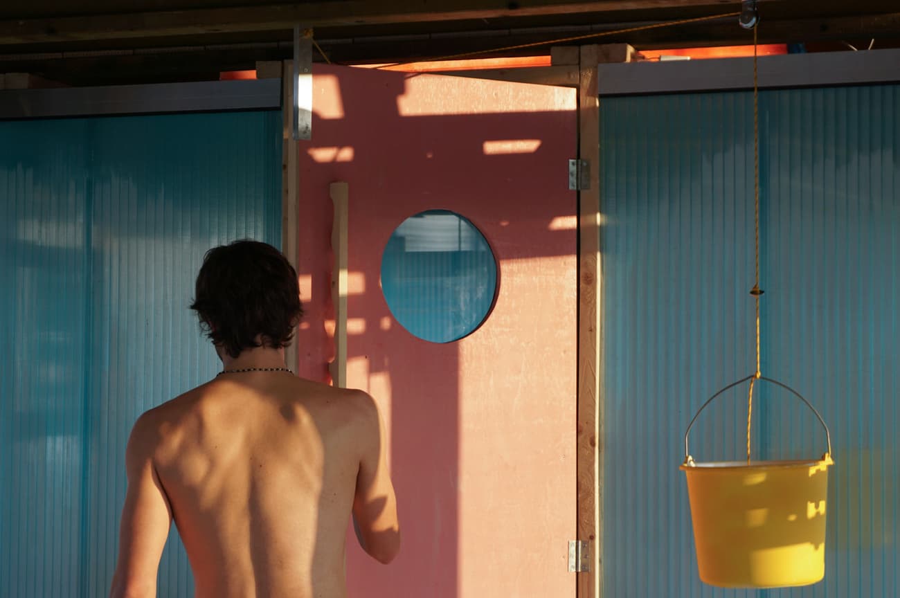 Architectural project - circular window, round window, pastel pink, light blue, natural materials, architectural detail, pink, wood, timber, playful design, colorful door, vibrant door, translucent panel, polycarbonate panel, outdoor space, wooden frame, timber frame, beach house, coastal style, summer house, relaxed vibe, casual style, Mediterranean influence, warm sunlight, natural light, shadow play, bohemian style, eclectic style, artistic touch, unique door, statement door, organic texture, corrugated panel, privacy screen, shading element, cottage feel, rustic touch, inviting atmosphere, outdoor living, passive design, eco-conscious, sustainable design, reclaimed materials, recycled materials, bold color, pastel colors, teal, yellow, plastic, glass, warm tones, natural tones