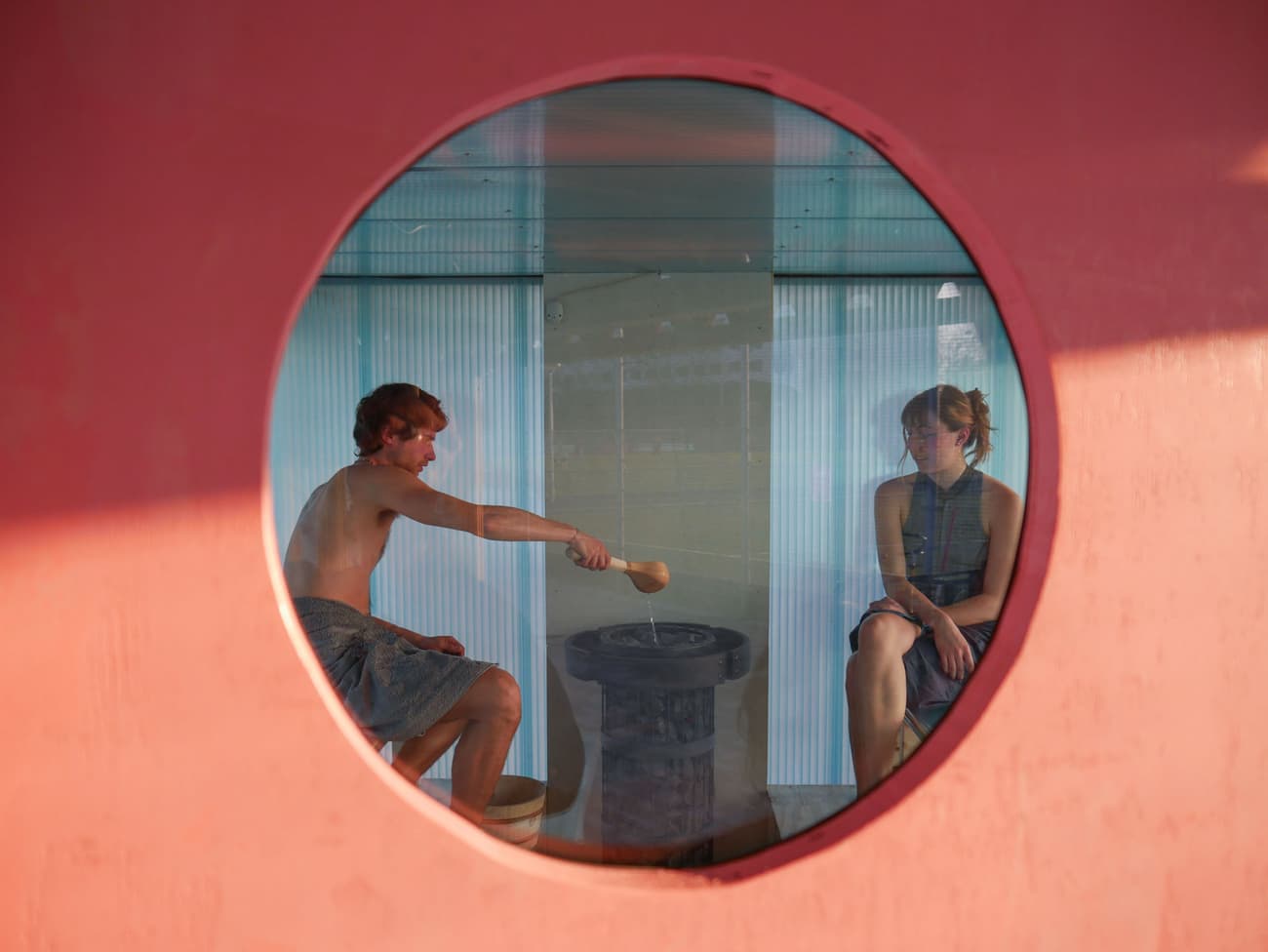 Architectural project - sauna, modern sauna, circular window, round window, pink wall, pastel pink, minimal design, minimalist, relaxation space, wellness space, spa design, cozy interior, warm interior, intimate space, serene vibe, calming atmosphere, light blue, translucent walls, indoor space, wellness retreat, spa retreat, natural materials, wood elements, wooden bench, relaxation zone, leisure area, architectural design, unique window, design focus, focus feature, light play, modern leisure, contemporary spa, architectural detail, soft lighting, tranquil space, interior view, serene environment, eco-friendly design, sustainable materials, health and wellness, pastel tones, pink, wood, timber, relaxation area