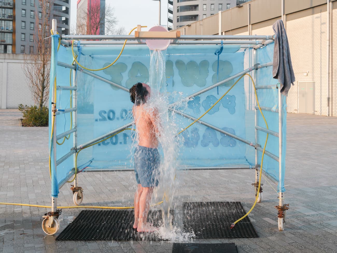 Architectural project - urban shower, temporary structure, minimal design, outdoor shower, unique concept, infrastructure, urban area, makeshift design, grey tones, scaffolding, outdoor bathing, city backdrop, urban setting, blue fabric, metal frame, experimental design, public shower, industrial design, urban intervention, experimental architecture, minimalistic structure, innovative use, exposed piping, urban experiment, raw materials, creative solution, urban installation, street context, unexpected space, city living, urban lifestyle, blue tones, steel, metal, fabric, playful design, utilitarian design, functional art, conceptual installation, cityscape