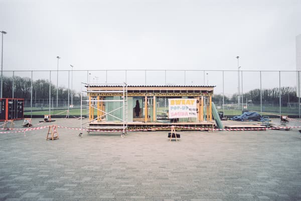 Architectural project - temporary structure, wellness space, wellness retreat, relaxation zone, leisure area, sustainable materials, timber, urban setting, innovative use, grey, metal, modular design, sustainable construction, community space, neutral tones, public installation, adaptable design, plywood, beige, light wood, modern aesthetic, functional design, pop-up sauna, outdoor sauna, eco friendly, urban sauna, Scandinavian influence, eco-friendly construction, minimalist architecture, contemporary design, prefab building, sleek lines, sports field backdrop, modern simplicity, open concept, industrial touch, portable architecture, temporary installation, outdoor activity, community wellness, Scandinavian style, relaxation, zen space, prefab construction, mobile sauna, casual setting, minimalist style, light brown