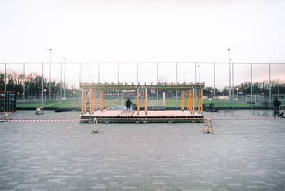Architectural project - wood, timber, temporary structure, urban setting, grey, metal, wooden frame, sustainable design, modular design, flexible design, urban park, neutral tones, public installation, urban environment, industrial vibe, sports venue, minimalist construction, multifunctional space, eco friendly, contemporary design, open framework, outdoor pavilion, public space, gathering area, metal mesh, community center, outdoor seating, event space, architectural assembly, field backdrop, adaptable structure, lightweight materials, social hub, outdoor venue, modern gathering, light construction, streamlined architecture