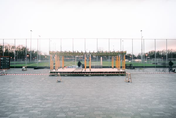 Architectural project - wood, timber, temporary structure, urban setting, grey, metal, wooden frame, sustainable design, modular design, flexible design, urban park, neutral tones, public installation, urban environment, industrial vibe, sports venue, minimalist construction, multifunctional space, eco friendly, contemporary design, open framework, outdoor pavilion, public space, gathering area, metal mesh, community center, outdoor seating, event space, architectural assembly, field backdrop, adaptable structure, lightweight materials, social hub, outdoor venue, modern gathering, light construction, streamlined architecture