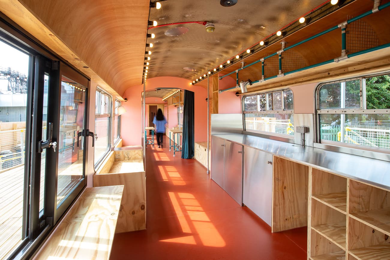 Architectural project - tiny house, portable home, flexible living, travel lifestyle, minimalist living, travel home, mobile living, red floor, vibrant floor, train conversion, bus home, tiny apartment, repurposed vehicle, metal interior, custom shelving, unique home, unusual dwelling, metal walls, rustic touches, warm interiors, reimagined interiors, creative dwelling, upcycled materials, recycled design, pink, city living, steel, metal, natural light, glass, exposed structure, innovative design, modern vibe, plywood, light wood, industrial style, multifunctional space, glass doors, casual space, adaptive reuse, urban design, creative space, warm wood, natural ventilation, light filled, eco friendly home, cozy vibe, open layout, outdoor connection, residential space, built-in seating, compact living, efficient layout, sliding doors, sustainable living, modern interior, urban home, wood interior, red, metal ceiling