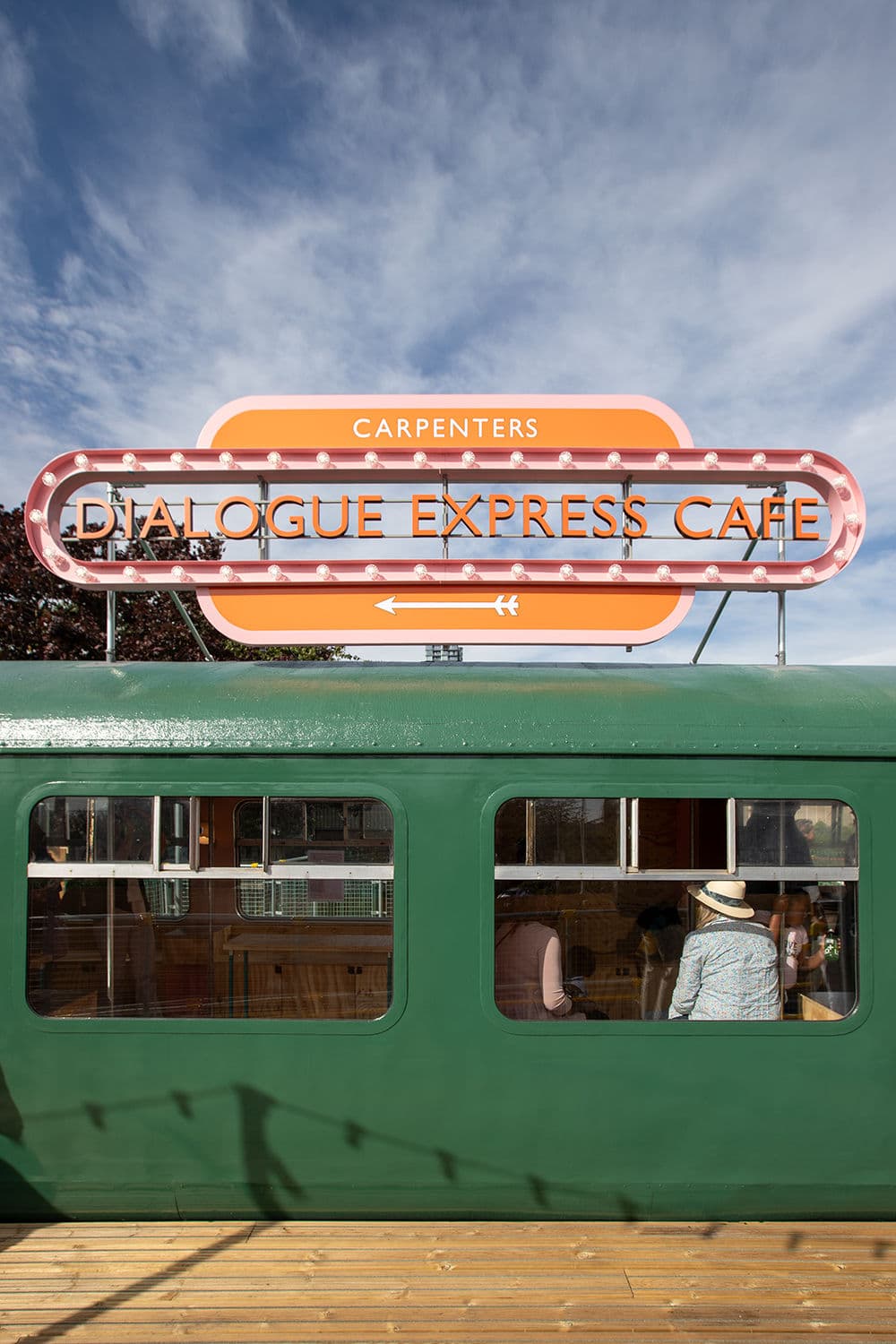 Architectural project - casual vibe, metal facade, retro vibe, bold colors, eclectic vibe, artistic vibe, quirky design, retro cafe, vintage cafe, train car cafe, neon sign, bright sign, pop color, colorful signage, green facade, train facade, funky style, playful atmosphere, urban cafe, city cafe, unique dining, nostalgia, classic train, diner style, casual hangout, creative aesthetic, edginess, bright pink, architectural reuse, city hangout, bright tones, pink, steel, metal, playful design, urban landscape, green, outdoor cafe, outdoor seating, adaptive reuse, vibrant colors, orange, industrial chic, open window