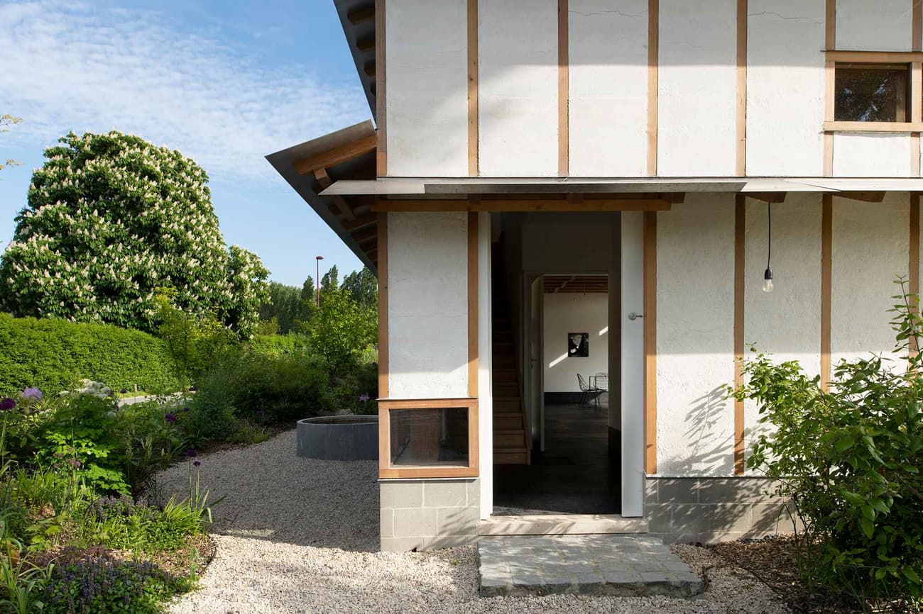 Architectural project - serene environment, wood, timber, outdoor space, natural light, passive design, warm tones, natural tones, green, neutral tones, daylight, beige, wood exterior, simple design, rustic charm, eco-friendly construction, green architecture, natural palette, biophilic design, sustainable home, natural ventilation, modern facade, timber cladding, cozy vibe, countryside home, plaster, warm atmosphere, organic materials, environmental design, garden design, rural setting, landscape design, greenery, lush garden, exterior view, eco house, gravel path, minimalist aesthetic, residential building, plaster walls, wooden structure, garden path, garden entrance, harmonized nature, seamless integration, light and airy, home design, cottage style, peaceful living, earthy textures, low impact