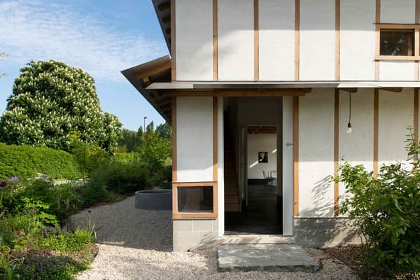 Architectural project - serene environment, wood, timber, outdoor space, natural light, passive design, warm tones, natural tones, green, neutral tones, daylight, beige, wood exterior, simple design, rustic charm, eco-friendly construction, green architecture, natural palette, biophilic design, sustainable home, natural ventilation, modern facade, timber cladding, cozy vibe, countryside home, plaster, warm atmosphere, organic materials, environmental design, garden design, rural setting, landscape design, greenery, lush garden, exterior view, eco house, gravel path, minimalist aesthetic, residential building, plaster walls, wooden structure, garden path, garden entrance, harmonized nature, seamless integration, light and airy, home design, cottage style, peaceful living, earthy textures, low impact