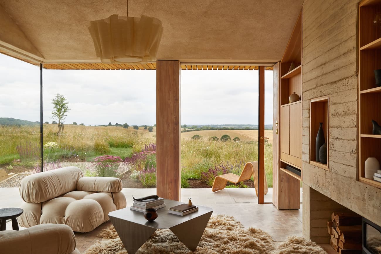Architectural project - natural materials, architectural detail, natural light, sustainable design, warm tones, timber structure, neutral tones, daylight, light wood, organic design, serene atmosphere, soft textures, eco-friendly materials, biophilic design, eco home, clean lines, indoor outdoor connection, Nordic style, landscape view, beige tones, panoramic view, inviting space, earthy tones, tranquil environment, modern living room, Scandinavian design, lounge chair, floor to ceiling glass, warm ambience, built-in shelving, shag rug, cozy living room, concrete fireplace, textured rug, plush seating, geometric table, natural elegance, home retreat, luxury living, design inspiration, open living room, sliding glass doors, wooden columns, minimalist interior, mid-century modern