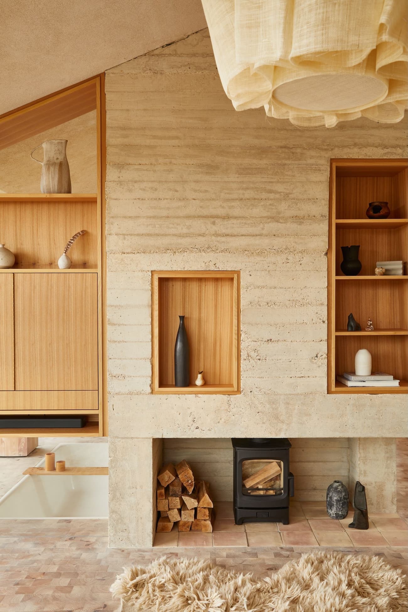 Architectural project - natural materials, soft lighting, eco-friendly design, wood, timber, inviting atmosphere, neutral tones, beige, brown, concrete, light wood, honey wood, natural textures, Scandinavian style, minimalist design, casual space, rammed earth, sustainable home, Nordic style, textured wall, warm ambiance, comfortable home, relaxed living, open plan, hygge style, modern fireplace, earthy textures, built-in shelving, warm living room, cozy living room, rustic living room, wood shelving, concrete fireplace, wood burning stove, firewood storage, decorative vases, rustic decor, bohemian vibe, shaggy rug, muted tones, ceiling pendant, tiles, linen, wool