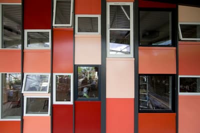Architectural project - thermal efficiency, colorful facade, colorful exterior, red facade, orange facade, pink facade, modern windows, black frame, black details, colorful cladding, panel cladding, vibrant design, modular panels, facade variation, lively exterior, exterior paneling, insulated panels, metal frames, red panels, orange panels, pink panels, contrasting colors, dynamic surface, ventilated facade, architectural color palette, pink, eco design, exterior design, geometric pattern, contemporary design, industrial touch, black, playful architecture, orange, construction detail, durable materials, passive house, white, energy efficient, sustainable facade, geometric facade, innovative facade, urban architecture, aluminum windows, modern exterior, public building, architectural rhythm, building envelope, architectural contrast, residential facade, square windows, urban style, red