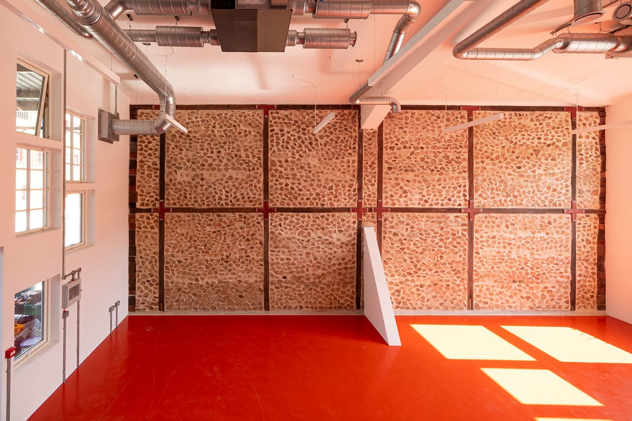 Architectural project - industrial transformation, raw elegance, workshop space, urban feel, contrasting colors, industrial interior, warehouse vibe, loft style, red floor, exposed ducts, creative studio, ductwork, vibrant floor, feature wall, accent wall, factory style, converted space, modern renovation, art studio, creative hub, building retrofit, architectural detail, raw materials, metal, natural light, sustainable design, eco design, exposed structure, industrial aesthetic, daylight, construction materials, multifunctional space, minimalist design, adaptive reuse, industrial chic, workspace, large windows, white, textured wall, stone, airy space, open plan, earthy tones, stone wall, bright interior, structural elements, high ceiling, urban style, red