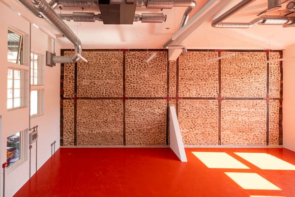 Architectural project - industrial transformation, raw elegance, workshop space, urban feel, contrasting colors, industrial interior, warehouse vibe, loft style, red floor, exposed ducts, creative studio, ductwork, vibrant floor, feature wall, accent wall, factory style, converted space, modern renovation, art studio, creative hub, building retrofit, architectural detail, raw materials, metal, natural light, sustainable design, eco design, exposed structure, industrial aesthetic, daylight, construction materials, multifunctional space, minimalist design, adaptive reuse, industrial chic, workspace, large windows, white, textured wall, stone, airy space, open plan, earthy tones, stone wall, bright interior, structural elements, high ceiling, urban style, red