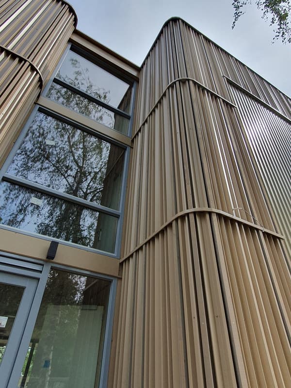 Architectural project - facade, contemporary exterior, vertical elements, metal cladding, ribbed facade, tall windows, architectural design, light play, shadow play, passive design, sustainable design, glass, warm tones, contemporary style, neutral tones, beige, structural design, building facade, architectural facade, daylight optimization, facade detail, minimalist design, exterior, urban design, natural ventilation, modern facade, corrugated metal, clean lines, large windows, energy efficient, glass windows, contemporary facade, modern style, urban architecture, modern exterior, vertical panels, reflective glass, eco facade, urban exterior