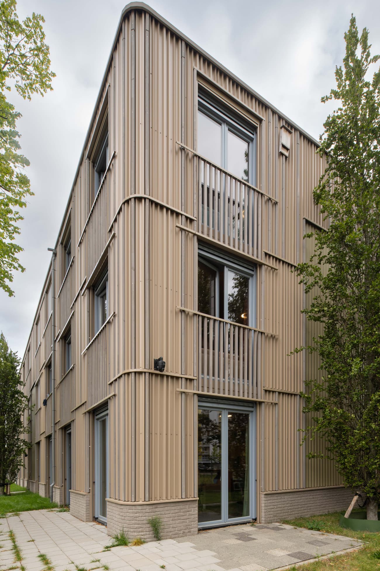 Architectural project - urban greenery, vertical lines, steel cladding, ribbed texture, landscaping, community living, minimalist, architectural design, eco-friendly design, steel, metal, outdoor space, green building, sustainable architecture, grey, neutral tones, urban development, city architecture, beige, daylight optimization, contemporary design, sleek lines, minimalist style, urban design, modern, low carbon, earth tones, natural palette, sustainable home, passive house, modern facade, large windows, energy efficient, greenery, garden view, residential building, green space, environmentally conscious, apartment building, smooth finish, exterior cladding, residential facade, urban living, city residence