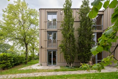 Architectural project - vertical elements, green facade, modern residence, tree-lined, eco-friendly design, wood, timber, outdoor space, eco-conscious, contemporary style, neutral tones, landscape architecture, light wood, natural setting, exterior, glass doors, eco building, green architecture, biophilic design, passive house, natural ventilation, modern facade, timber cladding, harmonious design, energy efficient, green living, nature-inspired, environmental architecture, nature integration, wood slats, wooden facade, residential building, sustainable facade, energy saving, urban nature, vertical cladding, wood architecture, architectural integration, sustainable living, apartment building