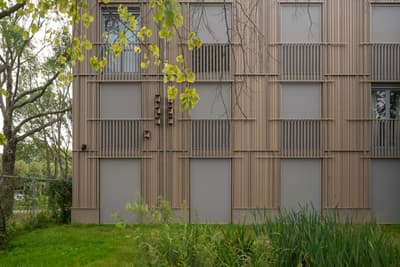 Architectural project - vertical rhythm, facade, beige facade, smooth texture, natural elements, slatted facade, building exterior, taupe, eco-friendly design, wood, timber, outdoor space, passive design, glass, eco design, contemporary architecture, exterior design, architectural facade, low carbon design, daylight optimization, modern design, urban oasis, peaceful setting, minimalist style, light brown, neutral palette, sustainable building, natural landscape, natural ventilation, modern facade, energy efficient design, architectural details, earthy tones, greenery, garden view, residential building, sleek design, calm atmosphere, green surroundings, vertical slats, soft colors, apartment building, muted tones, exterior cladding, city dwelling, urban living