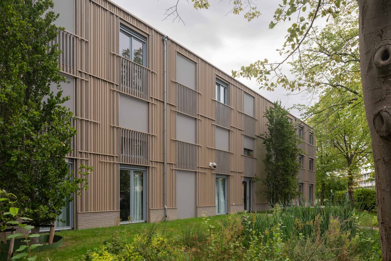 Architectural project - apartment facade, vertical elements, lush landscape, garden setting, curtain wall, natural materials, architectural design, wood, timber, metal, outdoor space, glass, contemporary style, grey, beige, wood facade, timber facade, exterior design, light wood, eco friendly, urban oasis, light brown, neutral palette, sustainable building, wood panels, green architecture, biophilic design, passive house, modern facade, large windows, energy efficient, earthy tones, brick, integrated nature, greenery, residential building, exterior wood, seamless integration, vertical cladding, simple lines, facade rhythm, natural surroundings, sustainable living, eco facade, urban living, modern residential