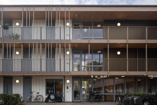 Architectural project - apartment facade, sustainable housing, metal railing, multi-story building, wooden details, warm facade, simple geometry, community living, eco-friendly architecture, bicycle friendly, shared spaces, natural materials, wood, timber, urban lifestyle, metal, glass, warm tones, innovative design, contemporary style, neutral tones, urban development, beige, brown, wood facade, timber facade, exterior design, light wood, daylight optimization, Scandinavian influence, neutral palette, minimalist design, passive house, natural ventilation, modern architecture, energy efficient, green living, residential building, balcony design, functional layout, modern living, vertical slats, architectural rhythm, urban housing