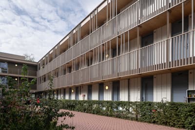 Architectural project - sustainable housing, residential complex, green facade, solar shading, inviting design, community living, housing development, shared spaces, rhythmic facade, minimal design, natural materials, eco-friendly design, wood, timber, outdoor living, passive design, warm tones, grey, beige, minimalist facade, light wood, functional design, daylight optimization, contemporary design, urban design, clean lines, timber cladding, modern architecture, energy efficient, beige tones, cozy atmosphere, wooden facade, vertical slats, apartment building, exterior space, urban living, street view, red, modern residential, communal space