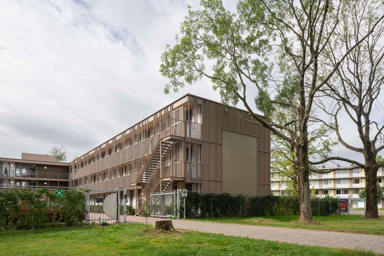 Architectural project - urban greenery, apartment block, metal railing, vertical lines, daylight design, compact layout, shared garden, communal living, architectural design, sustainable materials, city living, outdoor space, timber frame, eco-conscious, sustainable design, urban planning, wood facade, building facade, low carbon design, contemporary design, neutral palette, modular structure, modern aesthetics, prefabricated elements, green architecture, earth tones, natural ventilation, modern facade, landscape integration, energy efficient, environmental design, nature connection, eco-friendly building, residential building, passive solar, green space, courtyard, innovative architecture, brown tones, efficient design, exterior cladding, urban housing, modern residential, metal staircase