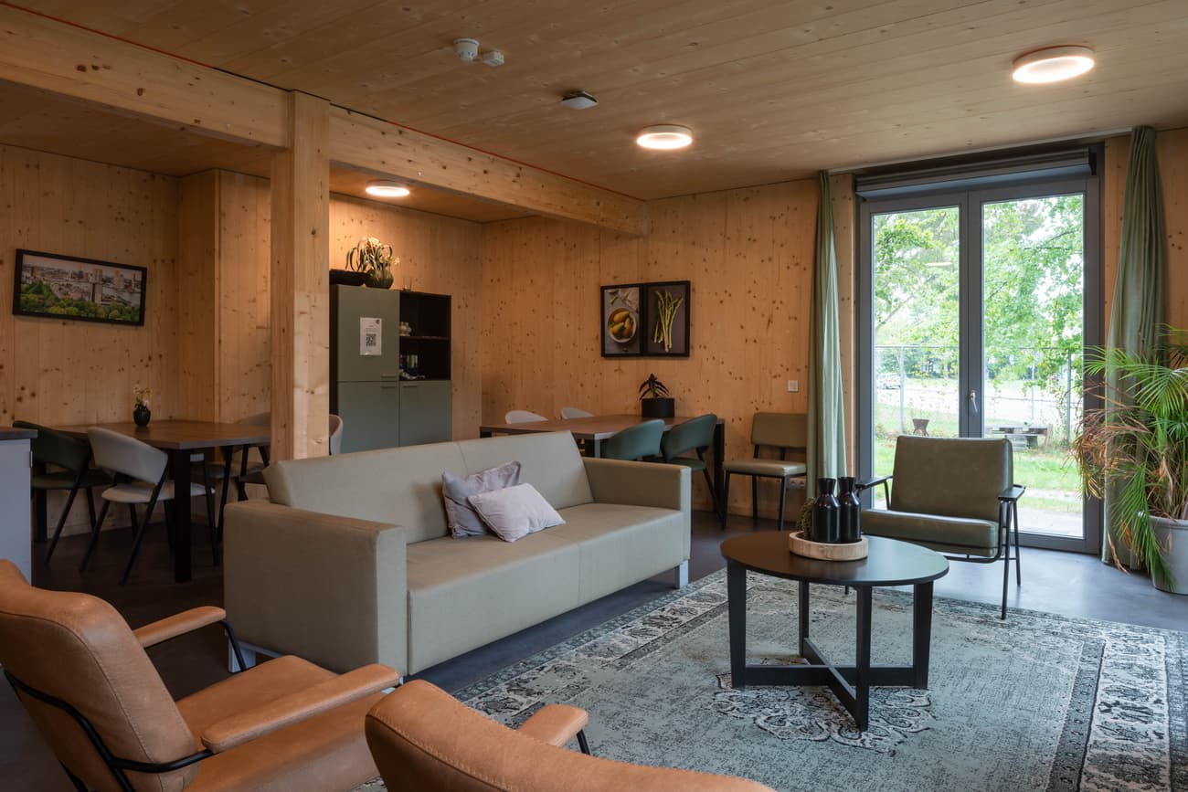 Architectural project - indoor greenery, living room, house plants, natural view, cozy lounge, warm interior, indoor space, wood, timber, natural light, inviting atmosphere, glass, warm tones, grey, green, neutral tones, daylight, beige, brown, light wood, rustic modern, minimalist vibe, Scandinavian style, casual seating, glass doors, timber walls, modern rustic, eco home, sustainable home, timber cladding, cozy vibe, Nordic style, relaxed living, casual living, residential design, lounge chairs, comfortable seating, sliding doors, home design, area rug, ceramic, family area, wood interior