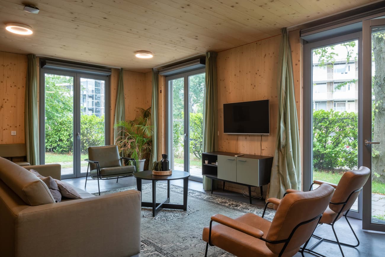 Architectural project - cozy living, living room, sitting area, warm interior, natural materials, timber, natural light, sustainable design, glass, natural tones, green, neutral tones, beige, brown, light wood, daylight optimization, rustic vibe, contemporary design, Scandinavian style, minimalist style, social space, relaxed atmosphere, gathering area, glass doors, timber walls, biophilic design, passive house, indoor outdoor, eco friendly home, comfortable home, casual living, open plan, inviting space, earthy tones, garden view, lounge area, warm living, simple decor, greenery view, wood paneling, modern interior, homey feel