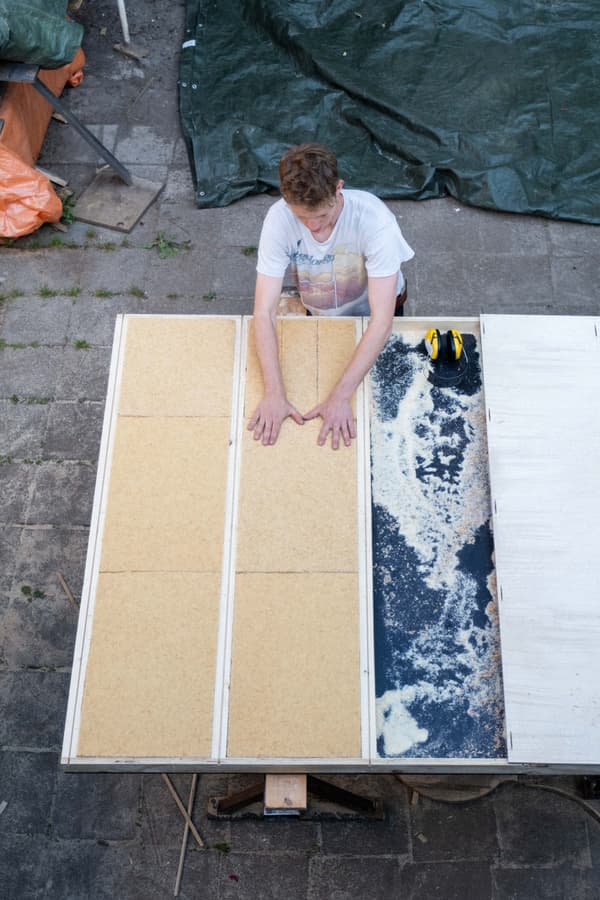 Architectural project - workshop, DIY project, hands-on, plywood sheet, particle board, builder, craftsman, manual work, workbench, sawdust, handmade, fabrication, outdoor workspace, maker space, assembly, woodshop, homemade, bespoke design, project table, DIY furniture, woodworking tools, workshop setup, renovation process, DIY construction, sustainable project, carpentry skills, rustic workshop, material preparation, off-white, green tarp, raw materials, grey, construction site, carpentry, plywood, industrial vibe, beige, brown, natural wood, eco materials, building process, wood panels, woodwork, white, wood texture, custom build, construction