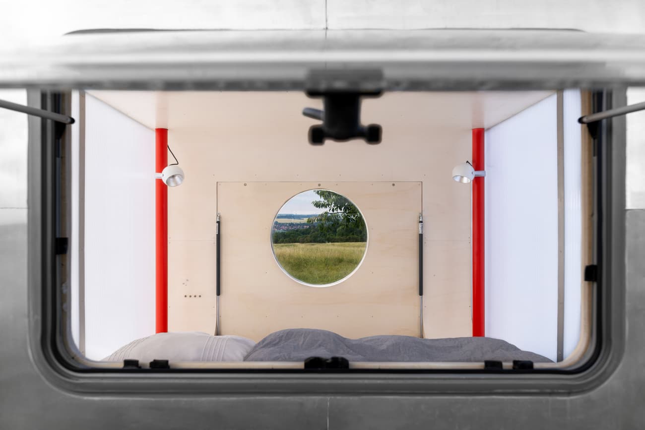 Architectural project - camper van, mobile home, tiny house, portable home, micro home, minimalist living, small bedroom, caravan interior, minimalist bed, cozy bed, nomadic living, travel home, red accents, red details, eco-friendly living, tiny home living, gray, circular window, round window, wood, metal, natural light, sustainable design, glass, warm tones, neutral tones, plywood, light wood, simple design, minimalist style, modern minimalism, white walls, indoor outdoor, white, cozy vibe, Nordic style, landscape view, energy efficient, small space, cozy nook, compact design, panoramic view, outdoor connection, bright interior, compact living, efficient layout, modern living, clean design, wood paneling, plywood interior, cozy bedroom, Scandinavian inspiration, pop of color, red