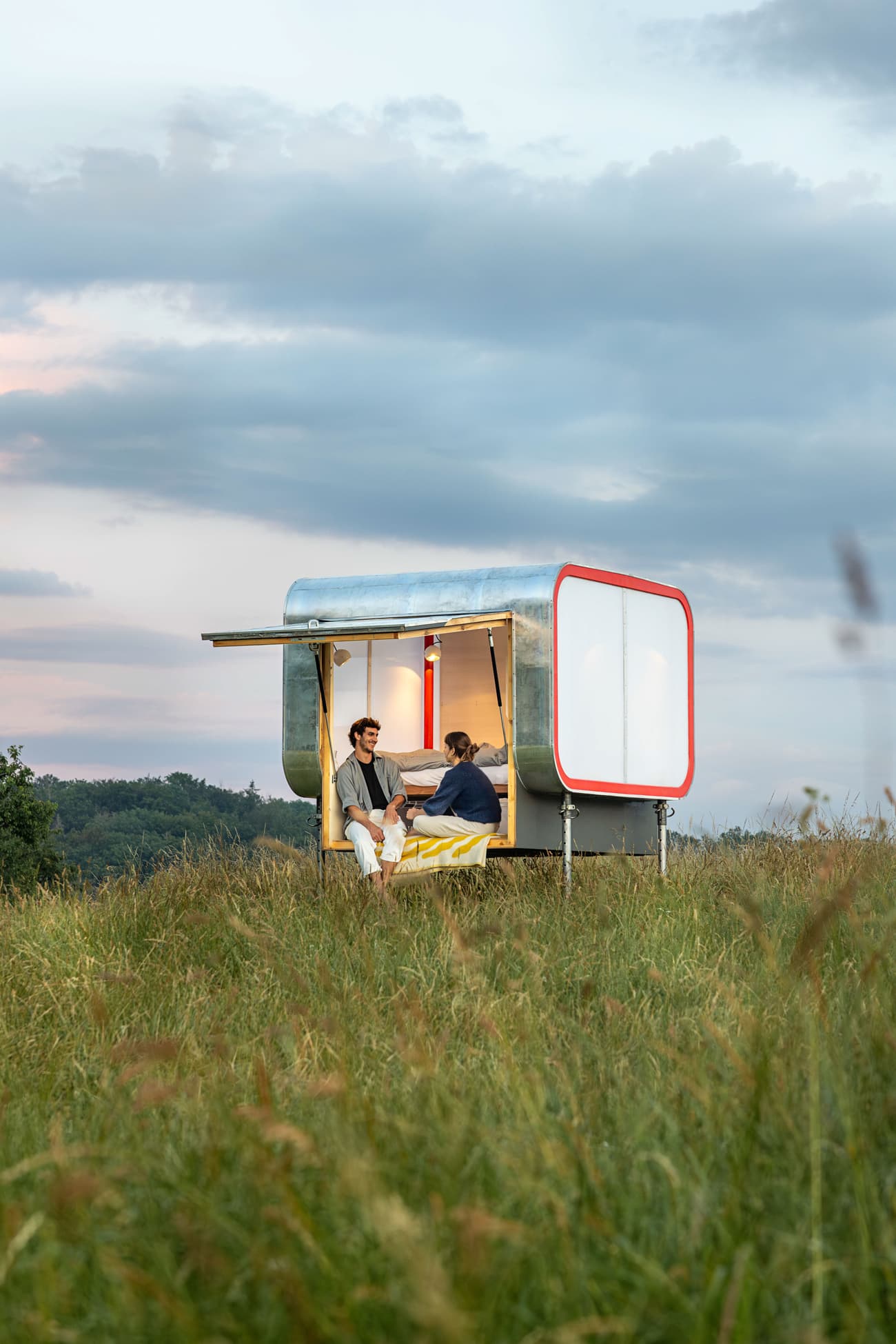 Architectural project - portable dwelling, mobile home, modern shelter, open hatch, rural escape, minimal impact, outdoor lifestyle, prefab structure, tiny cabin, small retreat, open countryside, metal structure, cozy living, contemporary cabin, natural backdrop, intimate moment, landscape setting, getaway cabin, temporary housing, intimate space, light blue, sustainable design, modular design, grey, lightweight design, evening light, multifunctional space, eco friendly, compact space, minimalist vibe, minimalist design, casual seating, relaxed atmosphere, steel frame, tranquil setting, adaptable space, white, wood accents, green living, compact design, countryside view, panoramic view, nature connection, rural setting, off-grid living, nature immersion, outdoor retreat, sky view, warm lighting, plywood interior, architectural innovation, red