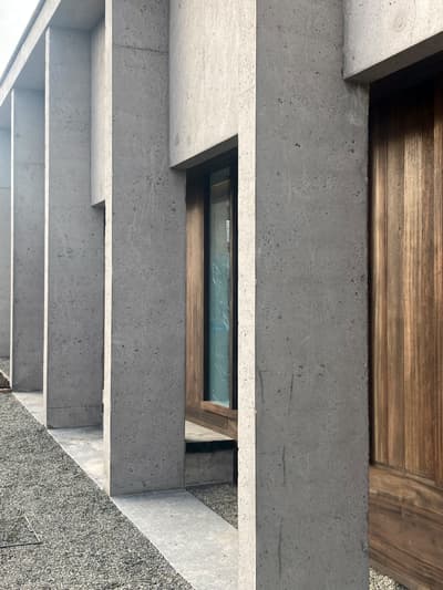 Architectural project - exposed concrete, geometric lines, raw concrete, vertical lines, grey facade, wooden doors, concrete facade, minimal vibe, grey concrete, brutalist architecture, brutalist, sustainable materials, wood, timber, outdoor space, sustainable design, modular design, grey, brown, concrete, architectural elements, exterior wall, industrial style, low carbon design, functional design, daylight optimization, natural textures, contemporary design, minimalist design, open facade, urban design, passive house, natural ventilation, modern facade, clean lines, architectural simplicity, energy efficient, wood accents, timber accents, earthy tones, eco-friendly building, sleek design, facade design, concrete wall, structural rhythm, contemporary building