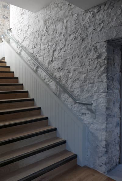 Architectural project - exposed stone, textured stone, rustic elegance, transitional space, country house, wooden steps, understated style, monochrome palette, white railing, classic design, rustic staircase, home staircase, residential stair, cozy interior, serene vibe, calming atmosphere, wood, metal, natural light, grey, neutral tones, beige, light wood, functional design, farmhouse style, simple design, architectural texture, warm wood, durable materials, modern rustic, textured surface, white, stone, inviting space, minimalist decor, traditional style, earthy textures, cozy home, tactile surfaces