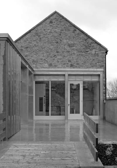 Architectural project - stone facade, stone exterior, vertical lines, exposed stone, modern barn, barn conversion, sliding glass, textural contrast, farmhouse vibe, entrance path, rectilinear form, natural materials, sustainable materials, wood, metal, passive design, glass, natural tones, eco design, grey, neutral tones, beige, concrete, industrial elements, rustic modern, natural textures, minimalist design, glass doors, adaptive reuse, clean lines, stone, compact design, stone wall, rustic facade, exterior view, gabled roof, residential building, concrete floor, simple lines, renovation, architectural contrast, exterior space