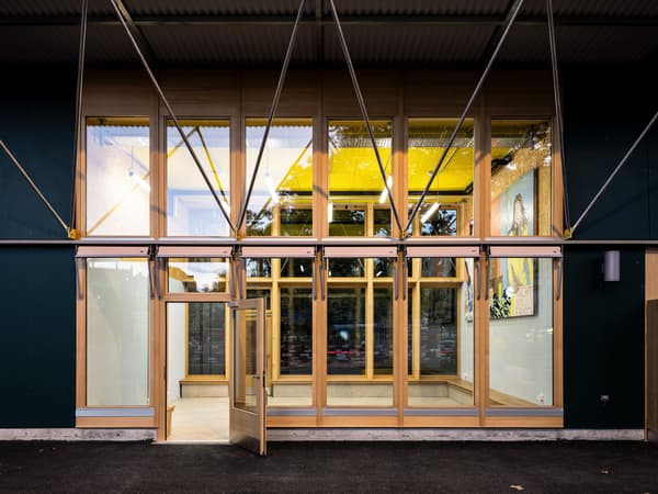 Architectural project - urban building, geometrical design, public access, community building, glass elements, transparency, exposed framework, materials emphasis, metal accents, welcoming entrance, wood, timber, steel, natural light, glass, warm tones, grey, neutral tones, timber structure, daylight, city architecture, beige, timber facade, architectural facade, modern aesthetic, engineered wood, functional design, eco friendly, contemporary design, industrial touch, sustainable building, modern facade, clean lines, modern architecture, compact design, exterior view, green design, eco architecture, minimalist exterior, sleek design, wooden structure, structural elements, public building, glass facade, urban vibe, architectural innovation, efficient space