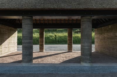 Architectural project - raw concrete, countryside vibe, earthy architecture, stone path, concrete columns, natural materials, raw materials, natural light, shadow play, passive design, sustainable design, warm tones, eco design, open structure, rural architecture, vernacular architecture, natural textures, outdoor pavilion, rammed earth, earth tones, earth construction, landscape integration, harmonious design, stone, open plan, shelter design, environmental design, rustic architecture, eco-friendly structure, rural setting, textured walls, natural ambiance, green design, pavilion design, open air, minimalist aesthetic, brown tones