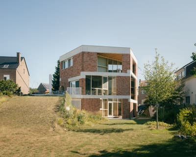 Architectural project - floor to ceiling windows, light wood accents, angular design, brickwork, architectural home, symmetrical design, minimal design, natural materials, timber, outdoor space, natural light, outdoor living, glass, warm tones, modern vibe, green, neutral tones, daylight, beige, concrete, exterior design, eco friendly, sustainable building, thermal mass, contemporary home, modern facade, clean lines, large windows, white, inviting home, modern architecture, energy efficient, open plan, brick, landscape design, brick facade, garden view, cozy exterior, family home, residential building, passive solar, suburban home, lawn area, urban home, geometric form, red