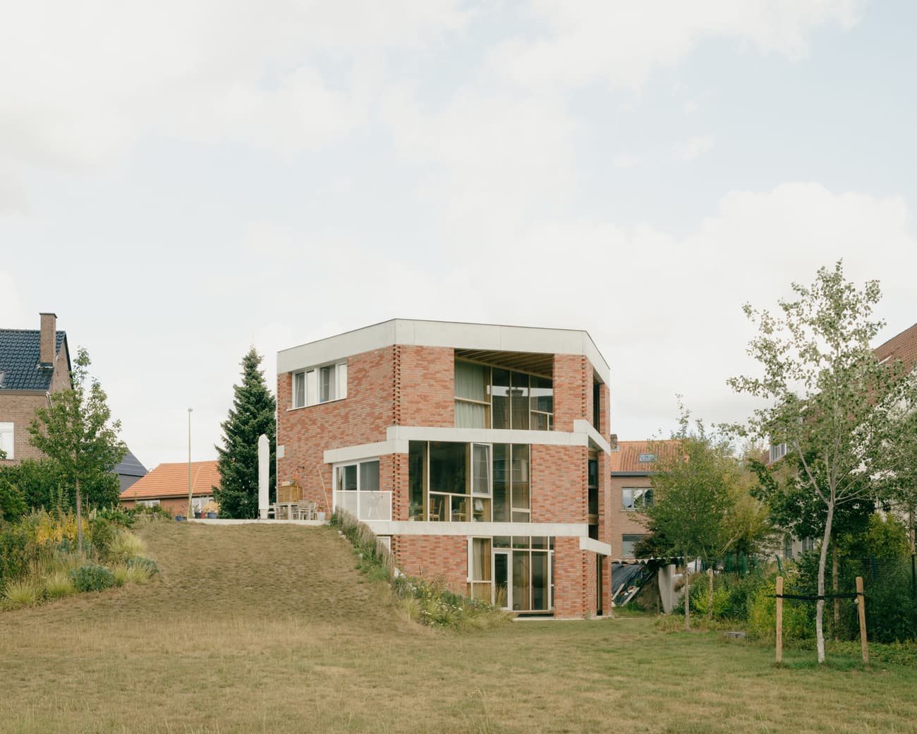Architectural project - facade, terrace, geometric shape, cubic form, brickwork, beige accents, brick house, patio, large openings, timeless style, backyard, landscaped garden, brick walls, white trim, brick cladding, lawn, eco-friendly design, outdoor space, natural light, glass, warm tones, concrete, exterior design, daylight optimization, minimalist design, natural palette, contemporary home, modern facade, landscape integration, large windows, open plan, residential design, red brick, garden view, residential architecture, private residence, family home, earthy textures, sculptural form, simple lines, concrete elements, suburban home, trees, sustainable living, indoor outdoor flow, modern house, architectural lines, urban living