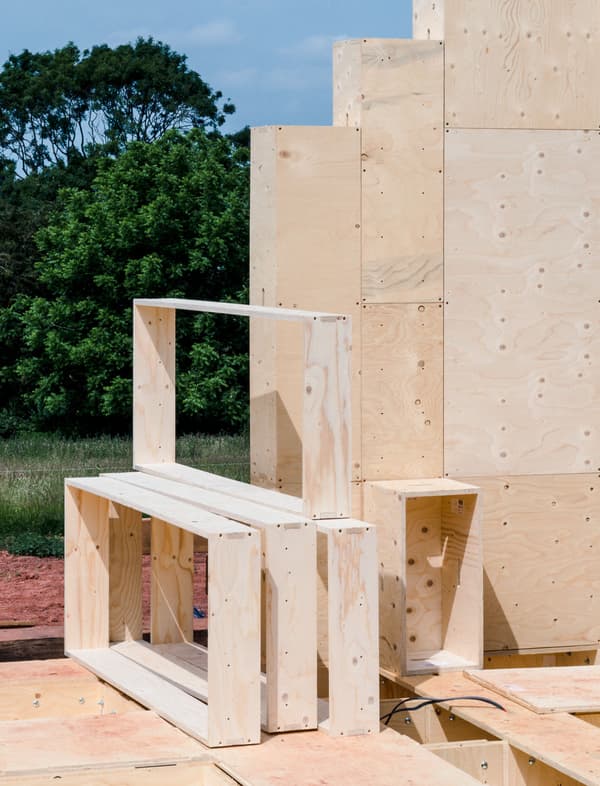 Architectural project - field setting, simple geometry, built environment, plywood structure, wood design, raw plywood, wood assembly, structural plywood, stacking design, creative structure, landscape interaction, yellow wood, assembly art, natural materials, sustainable materials, timber, functional art, outdoor space, natural tones, modular design, eco design, innovative design, architectural installation, outdoor installation, modern construction, plywood, beige, light wood, engineered wood, eco friendly, natural setting, timber construction, neutral palette, minimalist design, construction detail, prefabricated elements, low carbon, environmental design, landscape design, greenery, wooden panels, open space, texture play