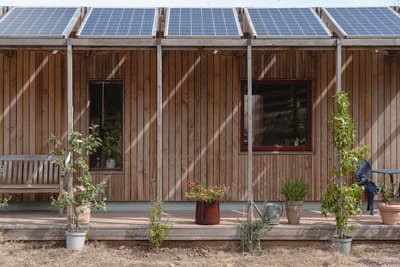 Architectural project - minimalist home, solar panels, solar energy, countryside style, country house, patio seating, wooden planks, veranda, plant pots, outdoor plants, energy conscious, cozy facade, perimeter garden, natural materials, wooden bench, wood, timber, steel, relaxed vibe, sustainable design, glass, green, neutral tones, timber structure, beige, brown, wood facade, low carbon design, eco friendly, wood exterior, natural setting, simple design, natural textures, eco home, passive house, natural ventilation, timber cladding, inviting home, timber house, energy efficient, rustic style, earthy tones, warm atmosphere, rustic facade, casual outdoor, rural setting, exterior view, green design, rustic home, wooden structure, vertical cladding, sustainable living, garden space