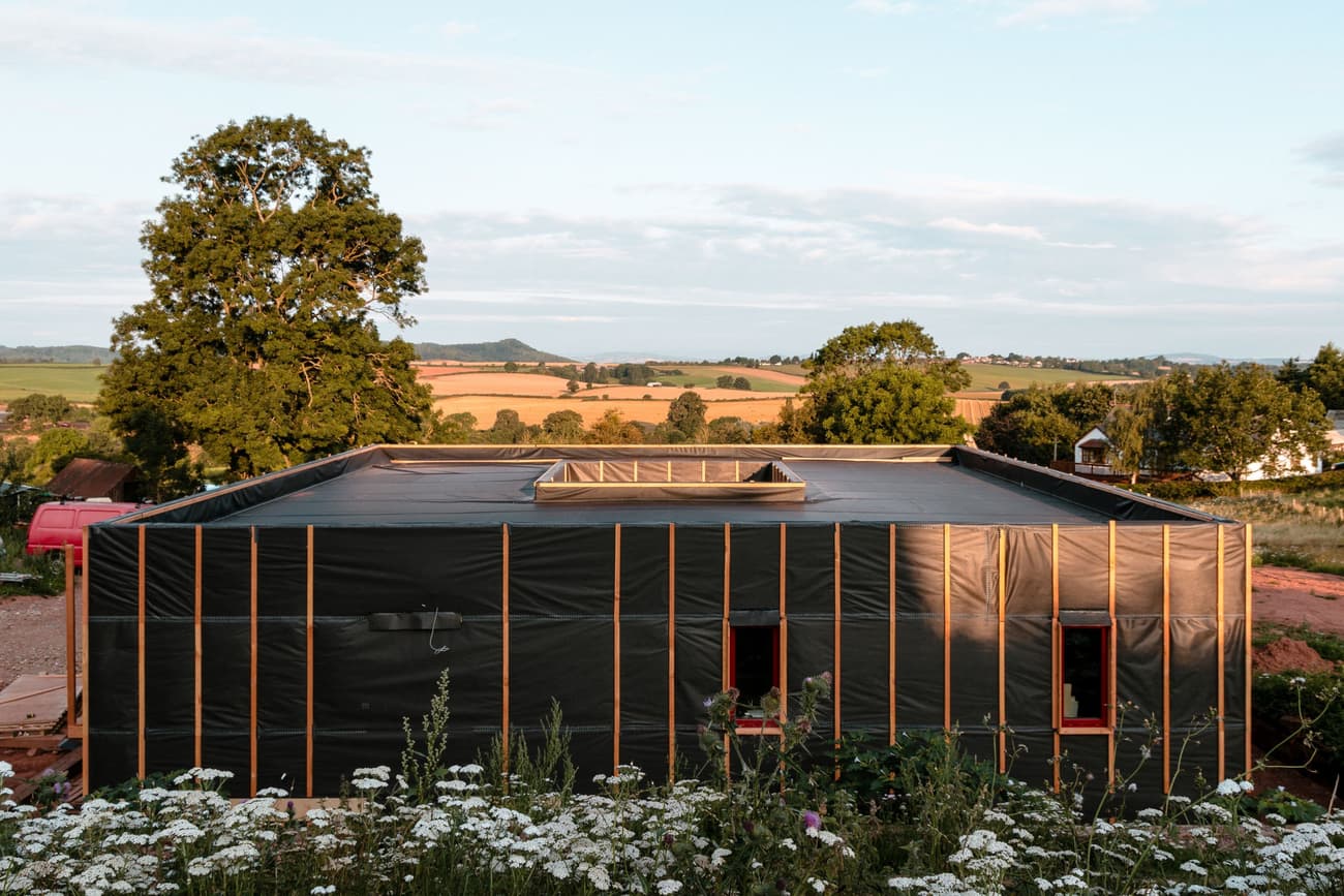 Architectural project - natural integration, rustic landscape, skylight roof, modern barn, contemporary rural, black facade, low carbon home, agricultural influence, natural materials, sustainable design, warm tones, modular design, sustainable construction, neutral tones, brown, minimal aesthetics, daylight optimization, flat roof, boxy design, simple design, minimalist architecture, black, field backdrop, eco building, eco construction, passive house, natural ventilation, scenic view, eco friendly home, countryside home, landscape view, energy efficient, open plan, countryside architecture, environmental design, outdoor connection, timber exterior, compact living, wooden slats, environmentally conscious, landscape harmony, rural house, rural retreat, nature setting, dark facade, geometric form