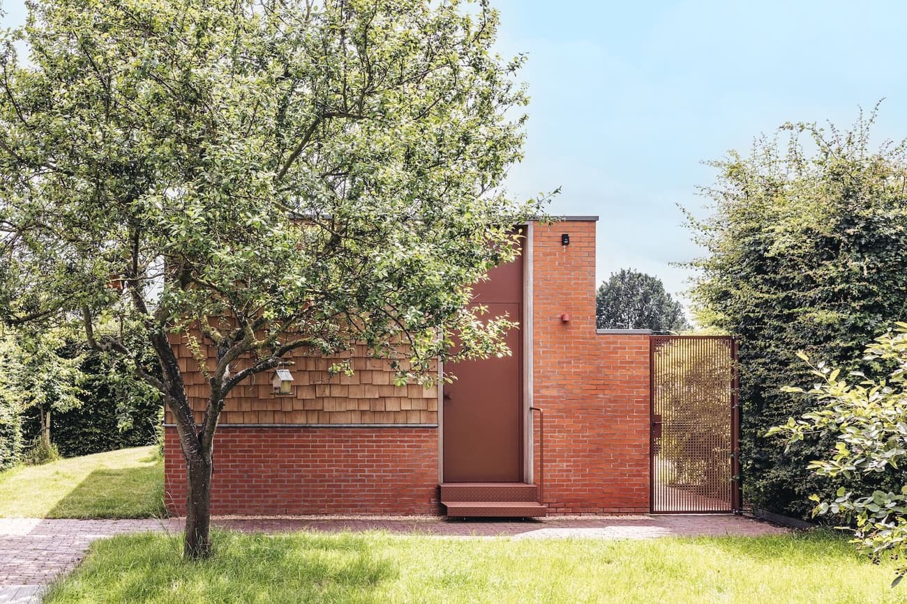 Architectural project - small house, green environment, garden house, green garden, red bricks, modern garden, outdoor path, timber details, natural materials, wood, timber, metal, outdoor living, sustainable design, warm tones, eco design, outdoor area, green, neutral tones, brown, minimalist facade, daylight optimization, natural setting, simple design, passive house, eco friendly home, cozy vibe, inviting entrance, wooden shingles, brick, landscape design, brick facade, backyard retreat, residential architecture, nature integration, shingle cladding, secluded home, rustic exterior, private garden, peaceful atmosphere, modern exterior, earthy colors, garden space, red